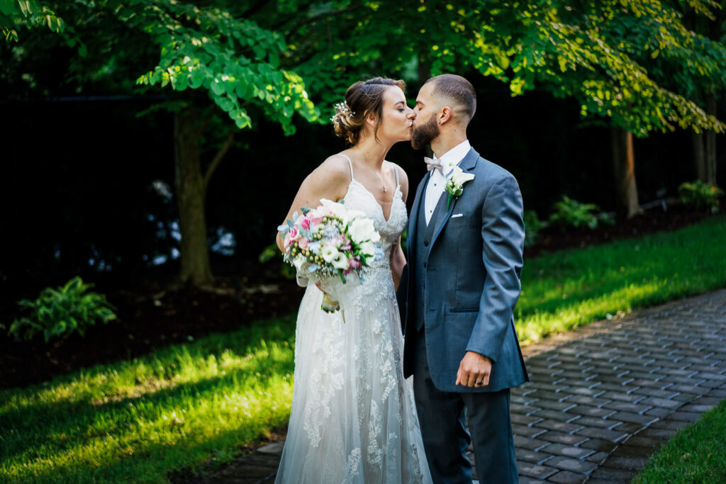 Newlyweds sharing first kiss on brick path surrounded by vibrant gardens at Tides Estate