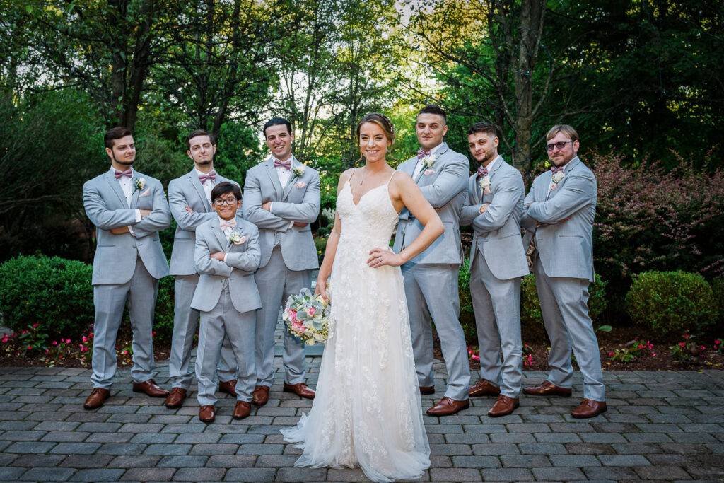 Bride standing confidently with groomsmen in gray suits on brick patio at Tides Estate