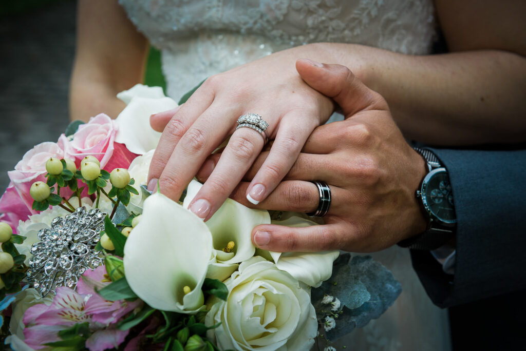 Close-up of wedding rings on bride and groom's hands resting on bridal bouquet with calla lilies and roses