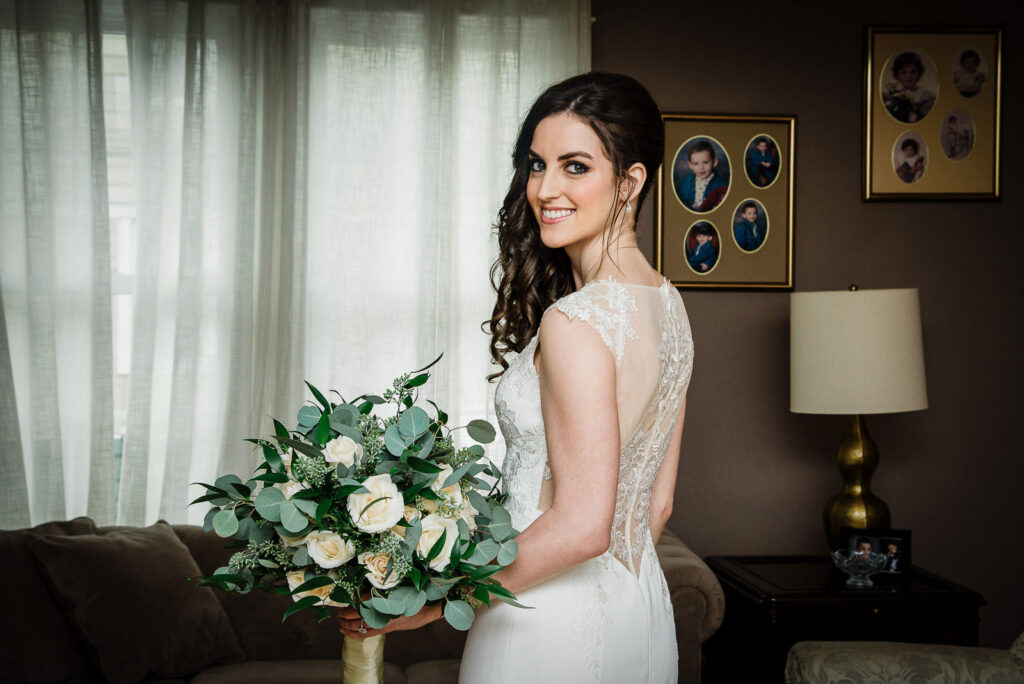 Bride smiling in fitted lace wedding gown with cap sleeves and greenery bouquet at Glen Cove wedding