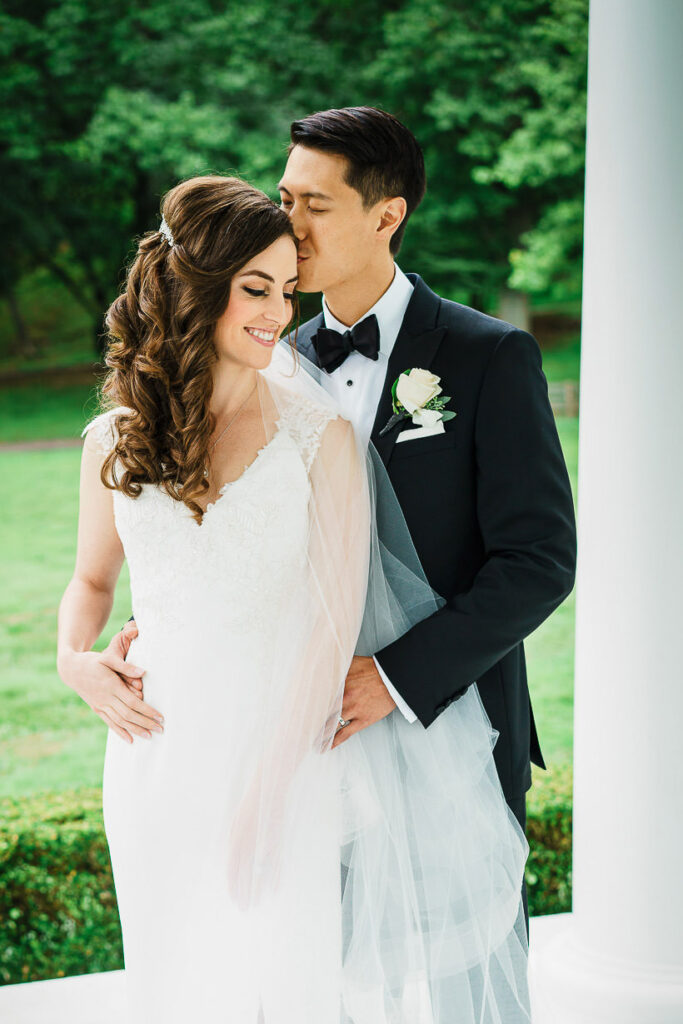 Romantic couple portrait under bride's cathedral veil with groom kissing bride's forehead on rainy wedding day