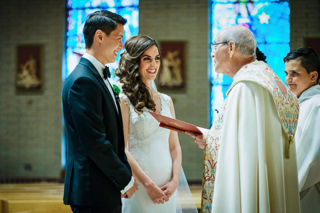 Bride and groom exchanging vows at altar during Our Lady of Hope Church Catholic wedding ceremony with stained glass backdrop