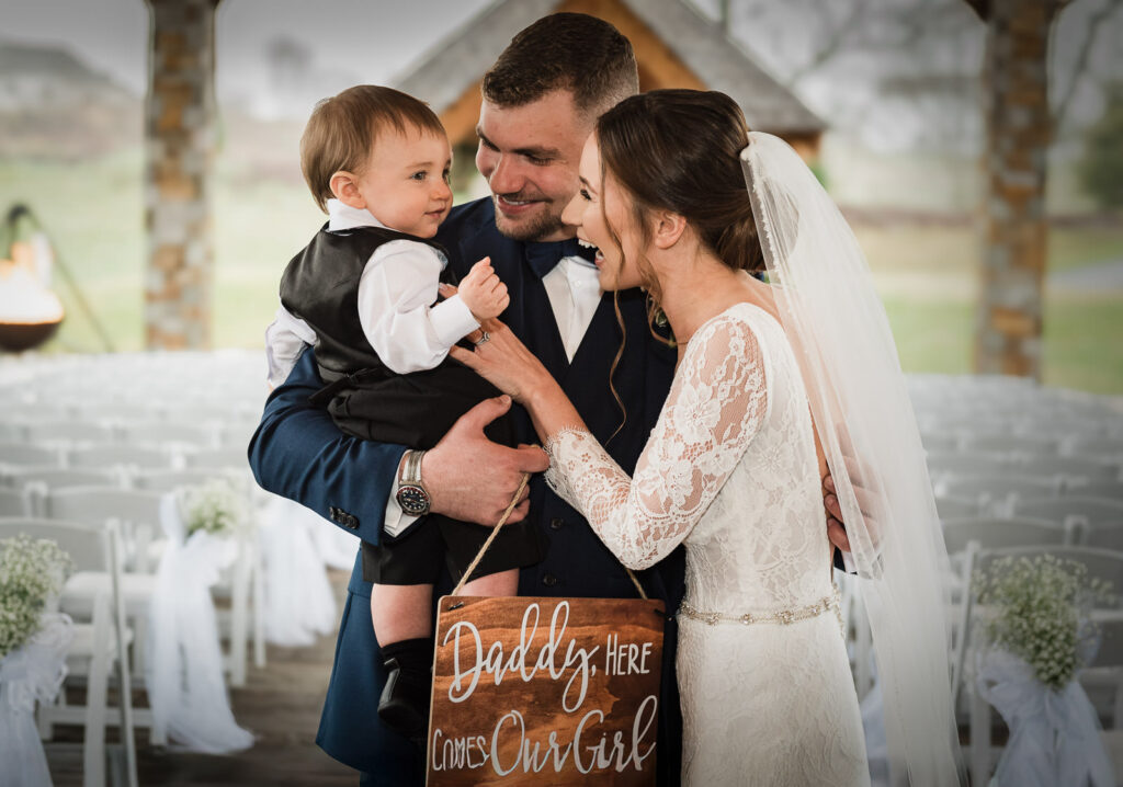 Newlyweds with young son holding wedding sign at Hamilton Farm Golf Club ceremony