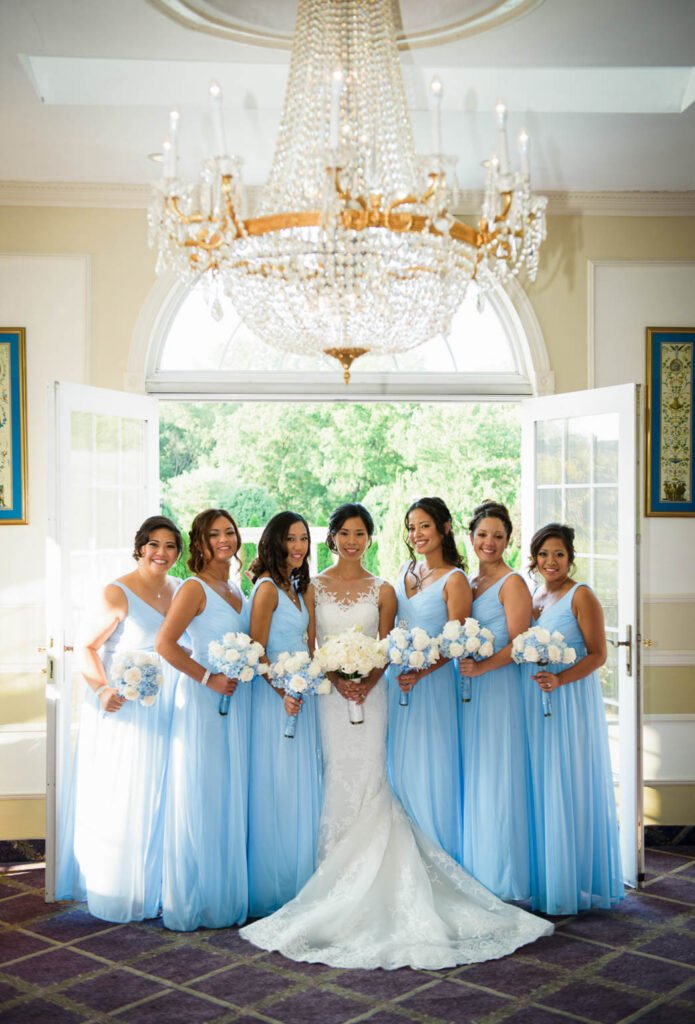 Bride with bridesmaids in light blue dresses under crystal chandelier at Rockleigh Country Club
