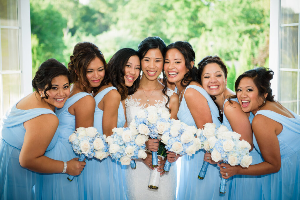 Bride with bridesmaids laughing with blue and white bouquets at Rockleigh Country Club