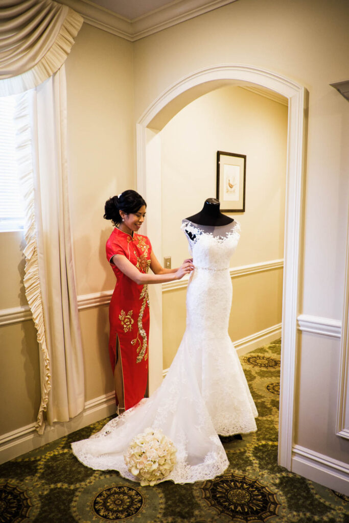 Bride in red Chinese qipao adjusting white wedding dress at Rockleigh Country Club