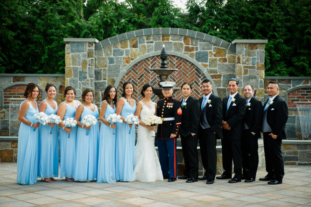 Full wedding party with Marine groom and light blue bridesmaids at Rockleigh Country Club stone fountain wall
