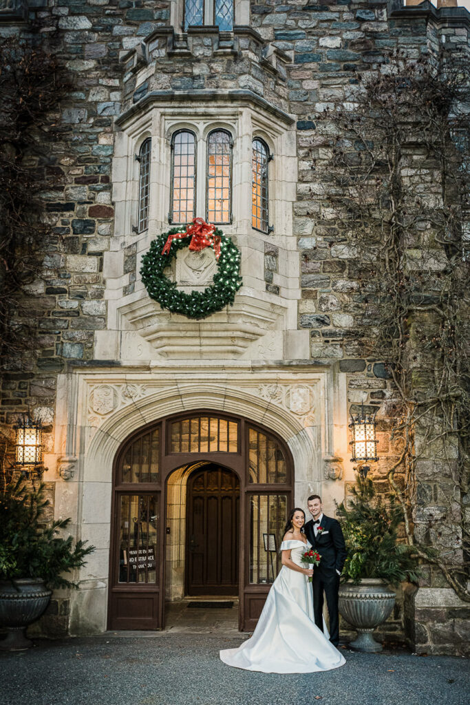 Bride and groom in front of Skylands Manor castle with holiday wreath