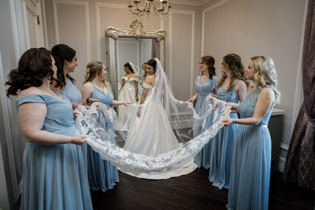 Bridesmaids helping bride with cathedral veil in bridal suite before wedding ceremony