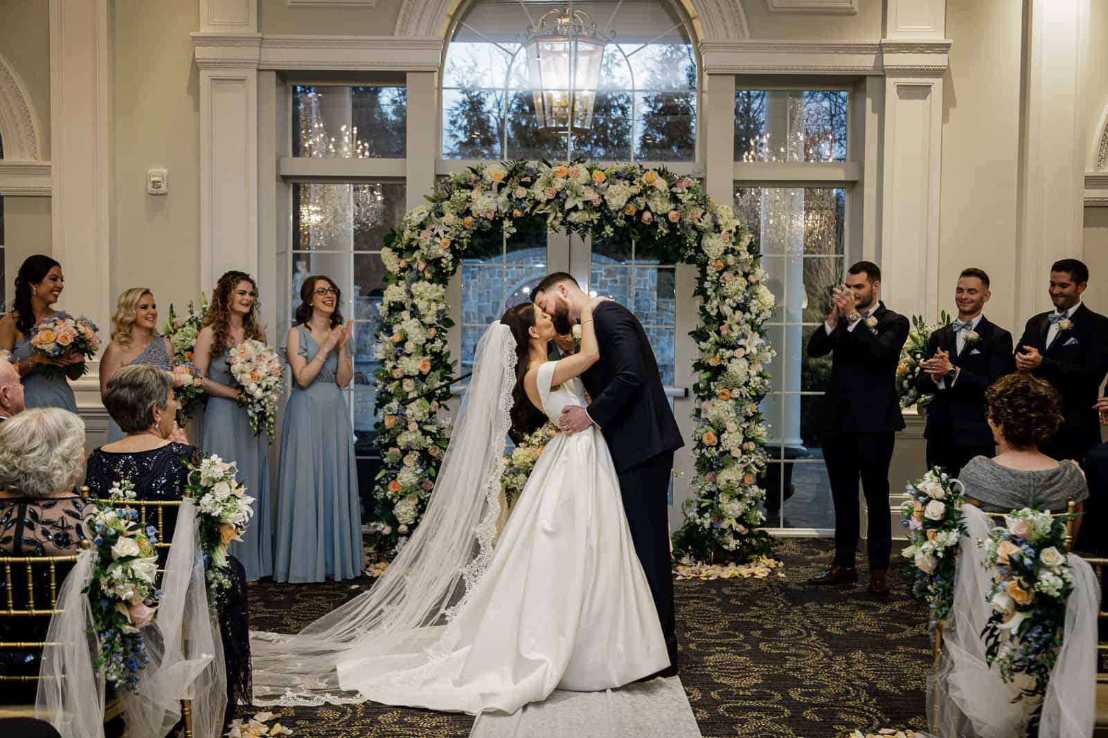 First kiss as married couple under floral arch at indoor winter ceremony