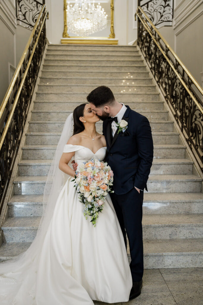 Newlyweds kissing on grand staircase at The Rockleigh winter wedding