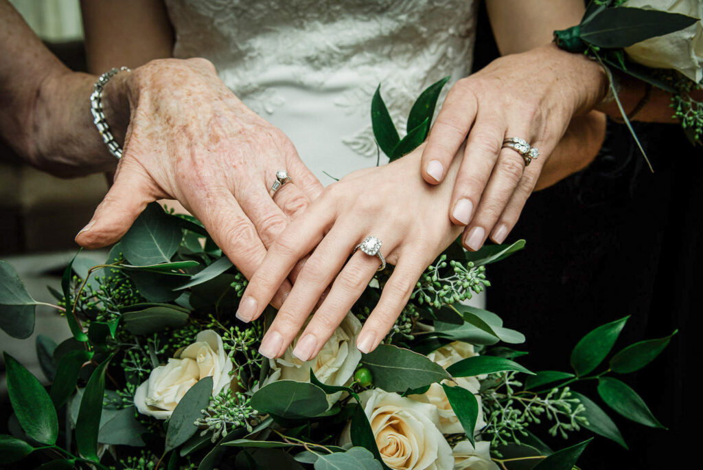 Three generations of wedding rings and engagement rings displayed on white roses and eucalyptus bouquet showing family legacy