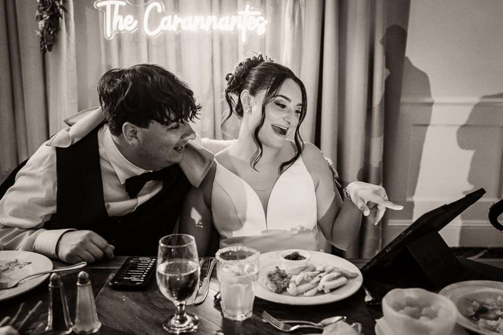 Bride and groom laughing as they look at their wedding photos on an iPad during the reception at The Mansion at Mountain Lakes, NJ