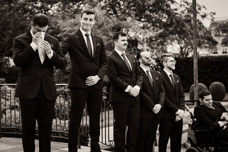 Emotional groom wiping tears while groomsmen look on during an outdoor wedding ceremony in New Jersey