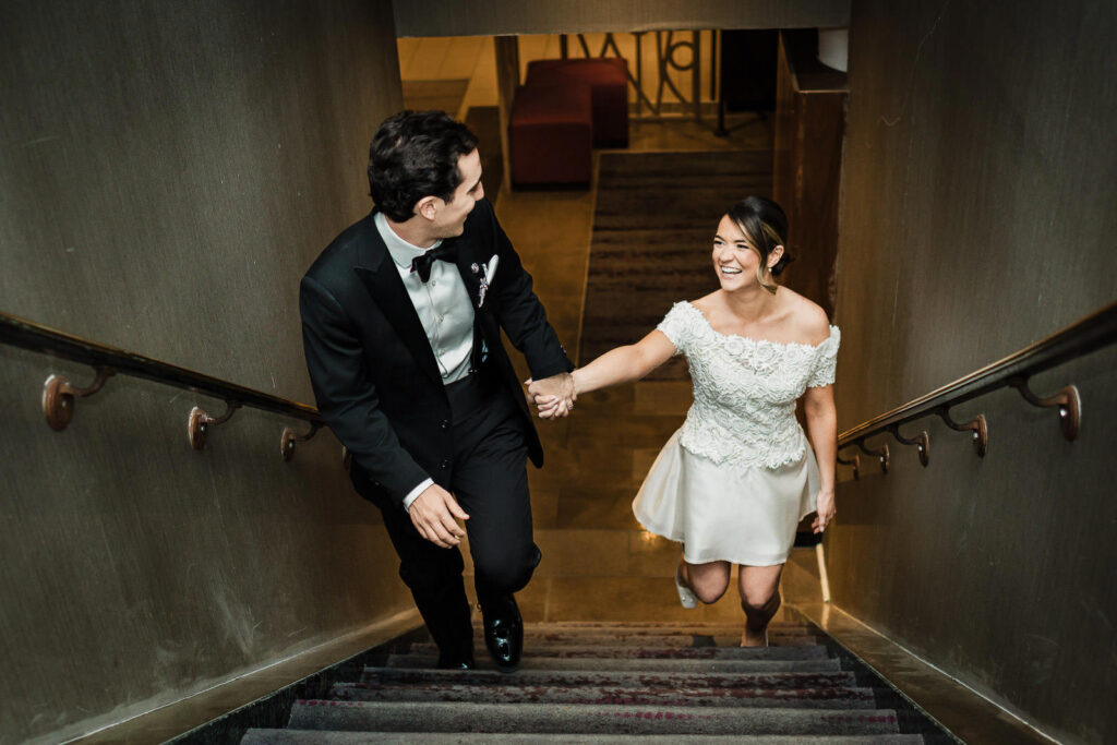 Bride and groom holding hands while descending staircase at Westin Governor Morris wedding reception in Morristown NJ