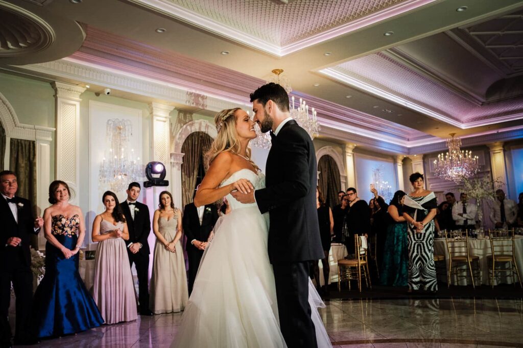 Bride and groom share an intimate first dance moment at Rockleigh Country Club in NJ, surrounded by guests and glowing crystal chandeliers under pink uplighting