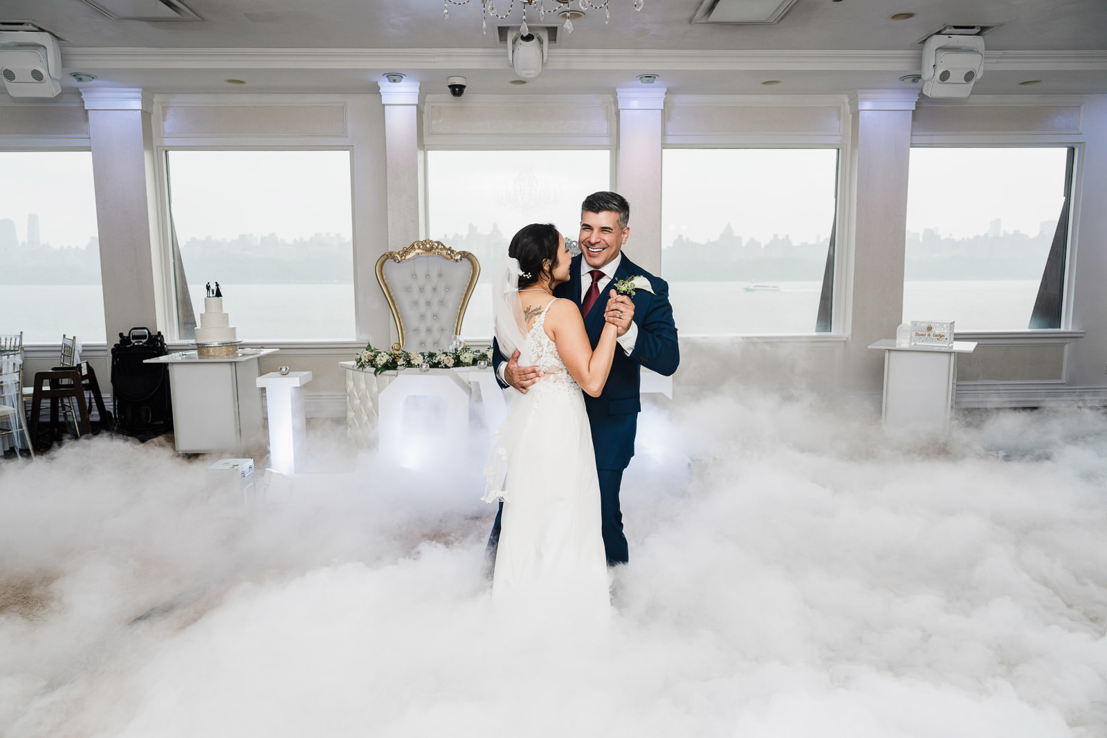 Groom laughing joyfully during first dance at The Waterside NJ, surrounded by low-lying fog machine clouds with the New York City skyline visible through floor-to-ceiling windows