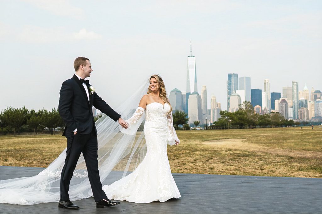 ride and groom walking with the NYC skyline at Liberty State Park