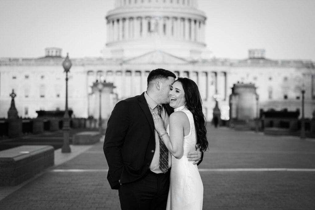 Black and white photo of man whispering to his laughing partner in front of the US Capitol Washington DC