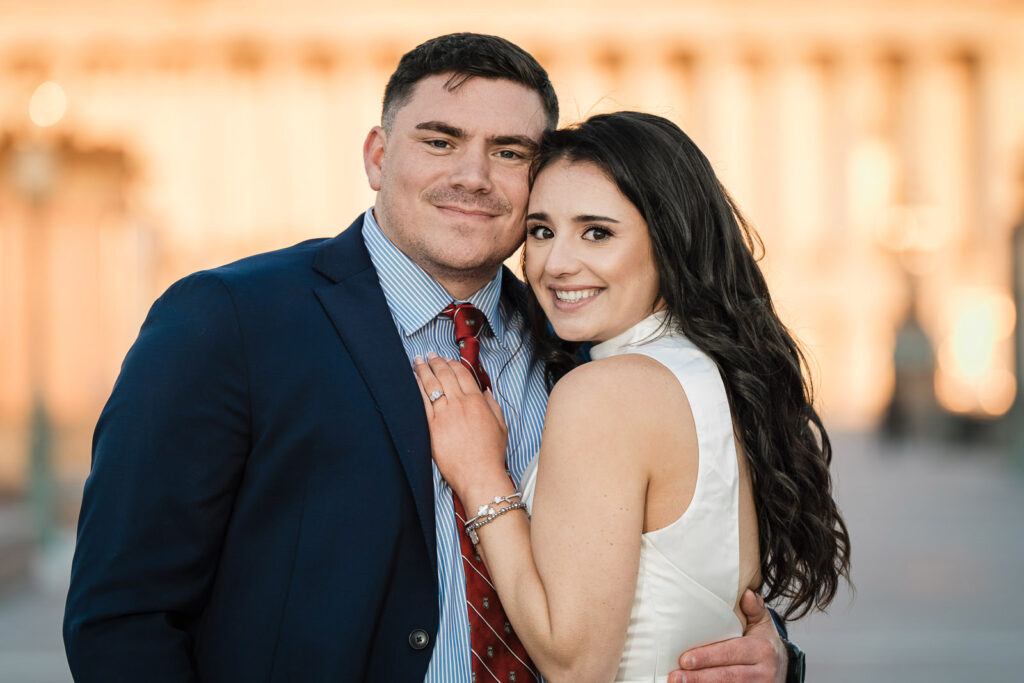 Close portrait of engaged couple in warm golden light with US Capitol columns behind them Washington DC