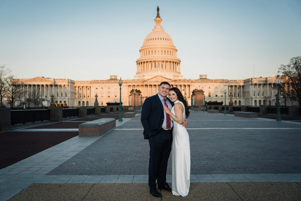 Engaged couple standing together in front of the Capitol dome bathed in golden sunrise light Washington DC