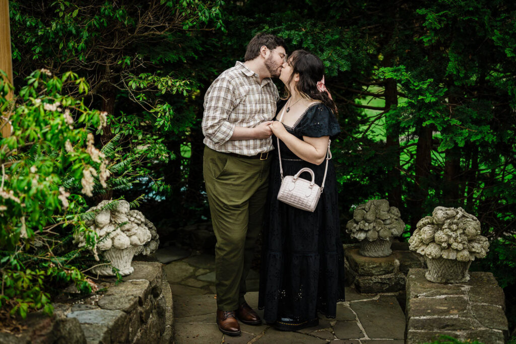 Couple kissing on stone garden patio flanked by ornamental urns at Reeves-Reed Arboretum Summit NJ