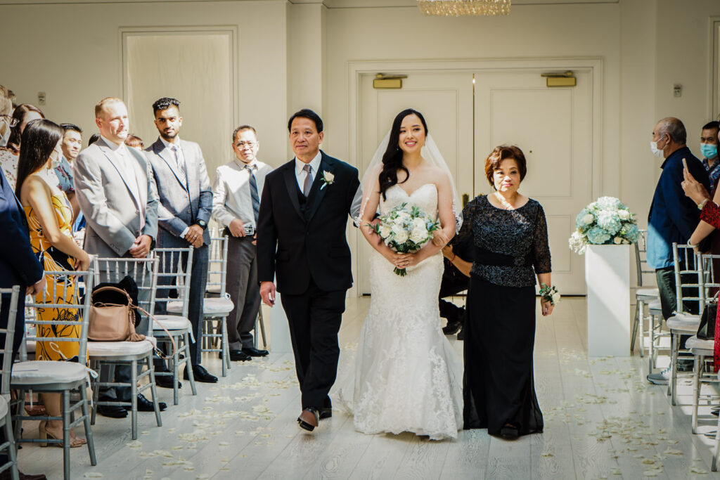 Bride walking down the aisle escorted by both parents during her Crystal Plaza wedding ceremony in Livingston NJ