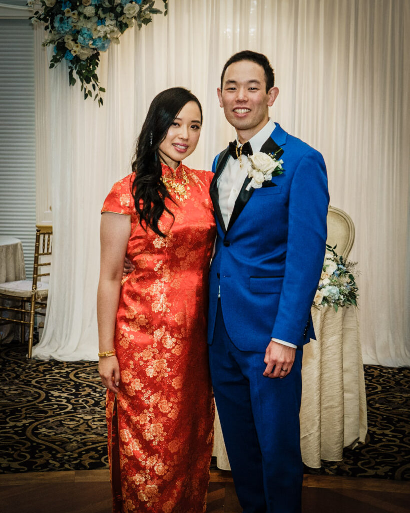Bride in red qipao and groom in blue suit posing together during their Crystal Plaza wedding reception in Livingston NJ