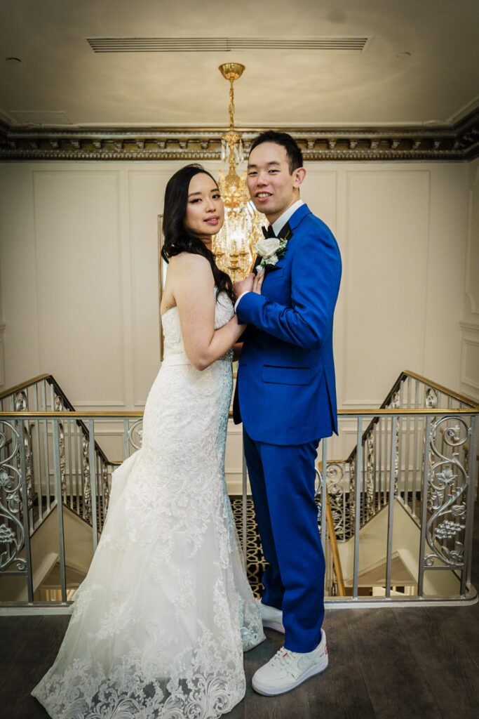 Bride and groom posing on the Crystal Plaza grand staircase with ornate gold and silver railings in Livingston NJ