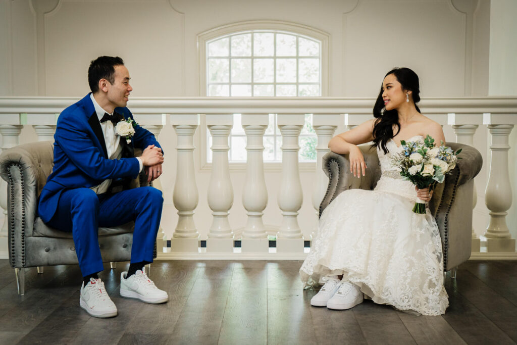 Bride and groom seated in velvet chairs on the Crystal Plaza mezzanine facing each other during their wedding portrait session in Livingston NJ