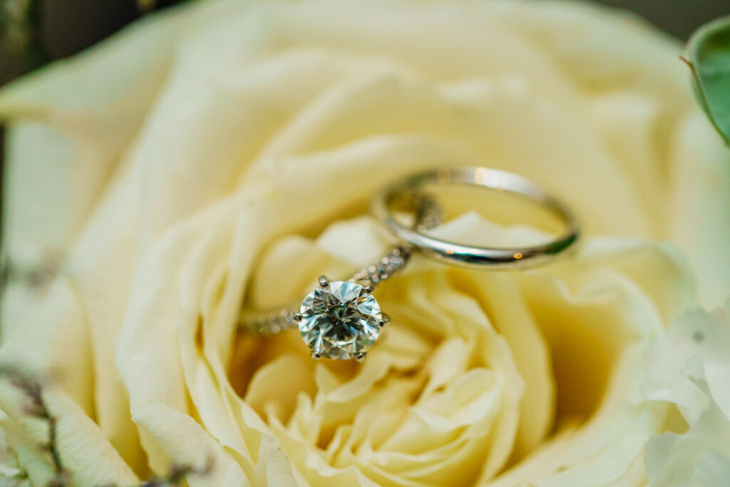 Diamond engagement ring and wedding band resting on a cream rose at a Crystal Plaza wedding in Livingston NJ