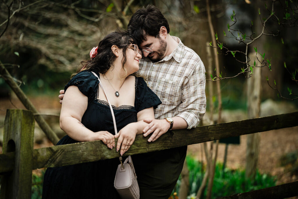 Newly engaged couple leaning together on rustic wooden fence at Reeves-Reed Arboretum in New Jersey