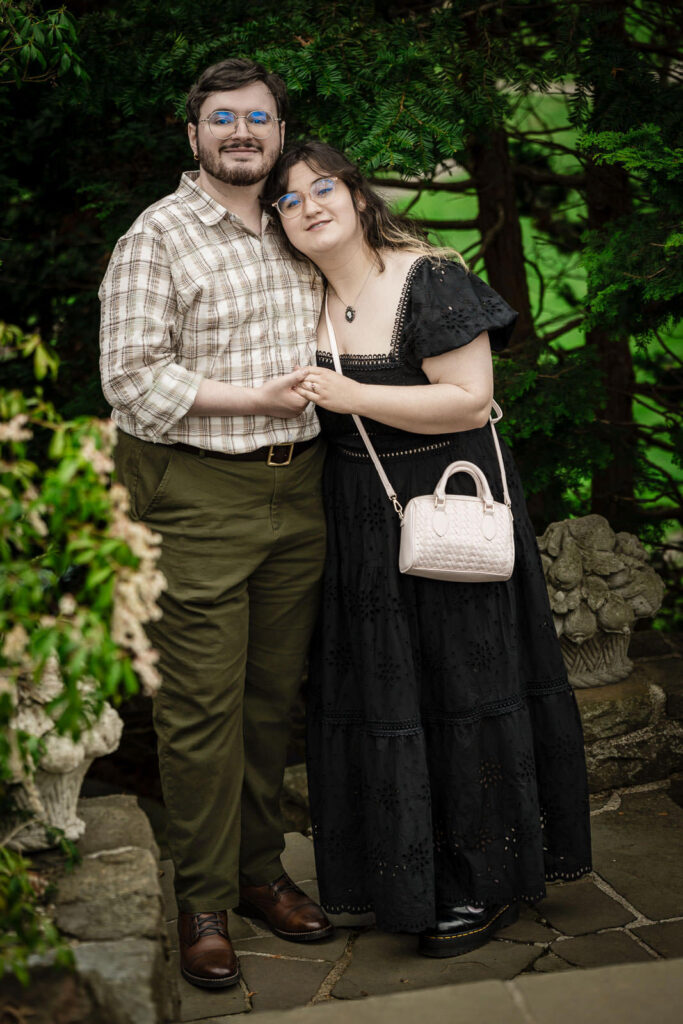 Engaged couple posing together on stone patio surrounded by lush greenery at Reeves-Reed Arboretum NJ