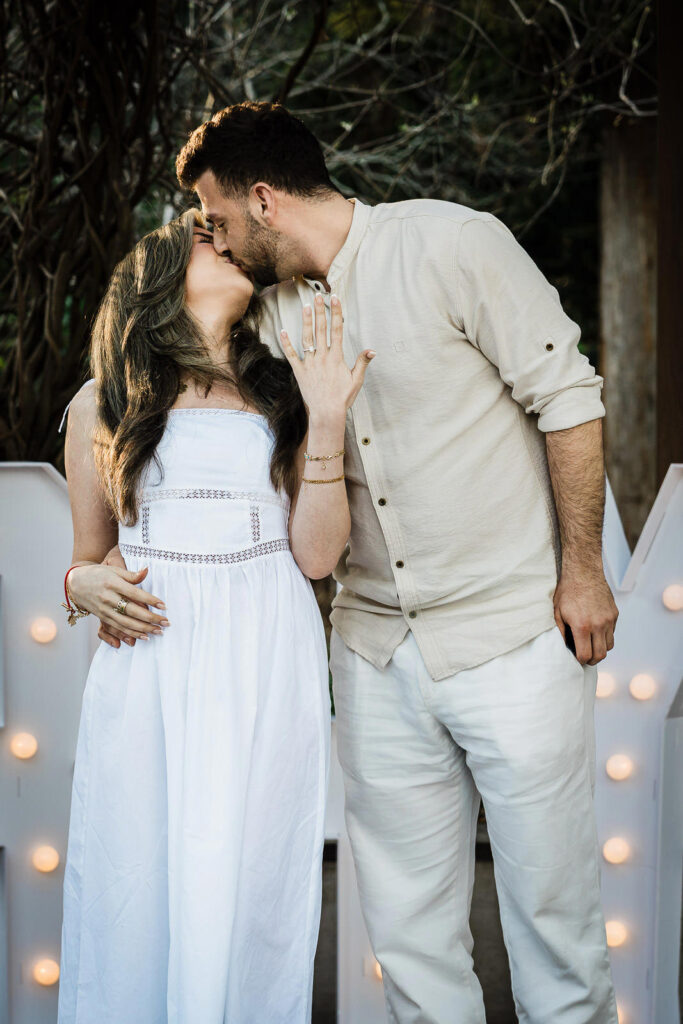 Couple kissing with engagement ring visible in front of marquee letters at Van Vleck Gardens NJ