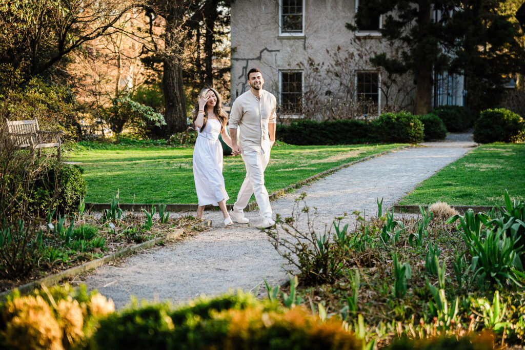 Couple walking hand in hand along sunlit garden path at Van Vleck House Gardens Montclair NJ