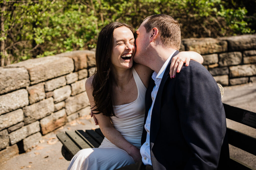 Couple laughing together on a bench in Fort Tryon Park near The Met Cloisters after engagement