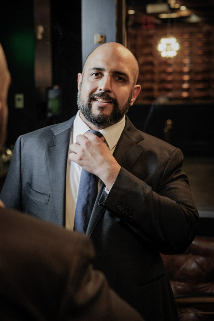 Groom adjusting blue tie with candid smile while getting ready at Crystal Plaza multicultural wedding