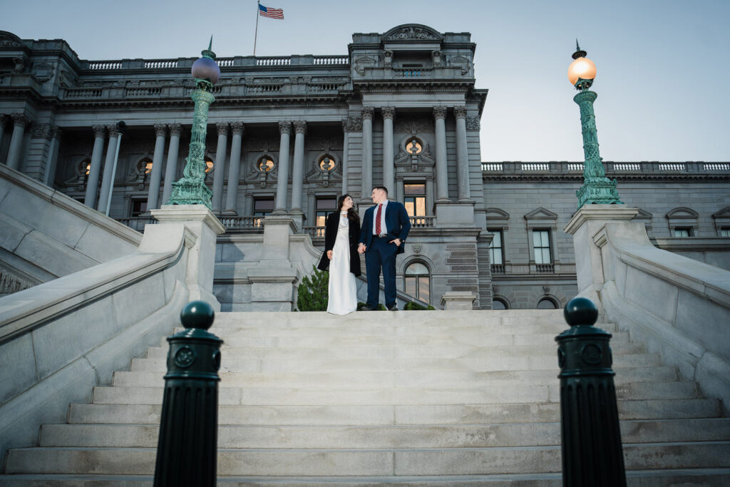 Couple standing on Library of Congress steps holding hands with American flag overhead Washington DC