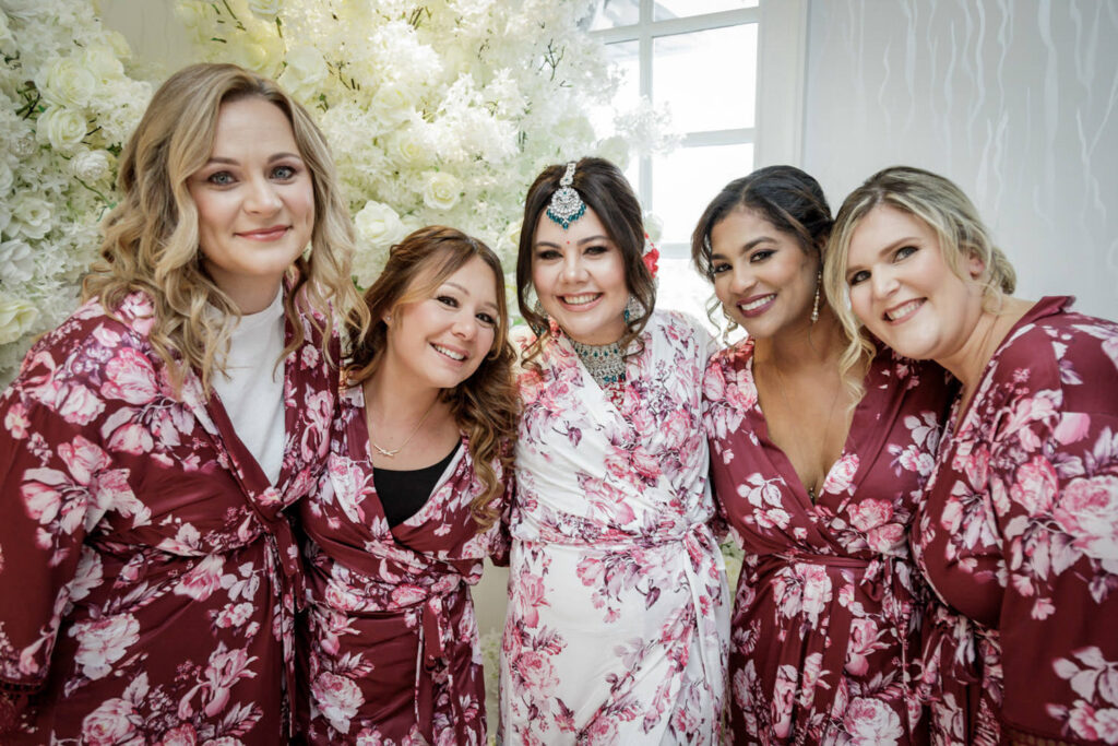 Smiling Indian bride surrounded by bridesmaids in matching floral robes at Crystal Plaza bridal suite