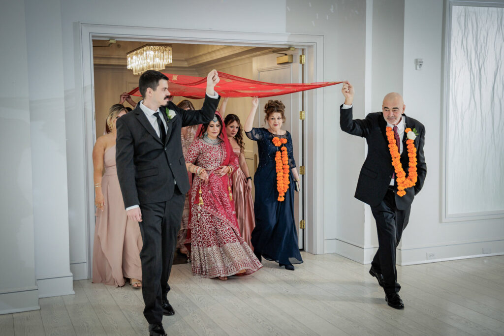 Indian bride walking under red dupatta held by family members during traditional bridal procession at Crystal Plaza