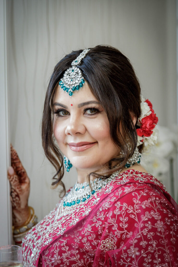 Close portrait of Indian bride wearing teal maang tikka henna covered hands and floral hair accessories