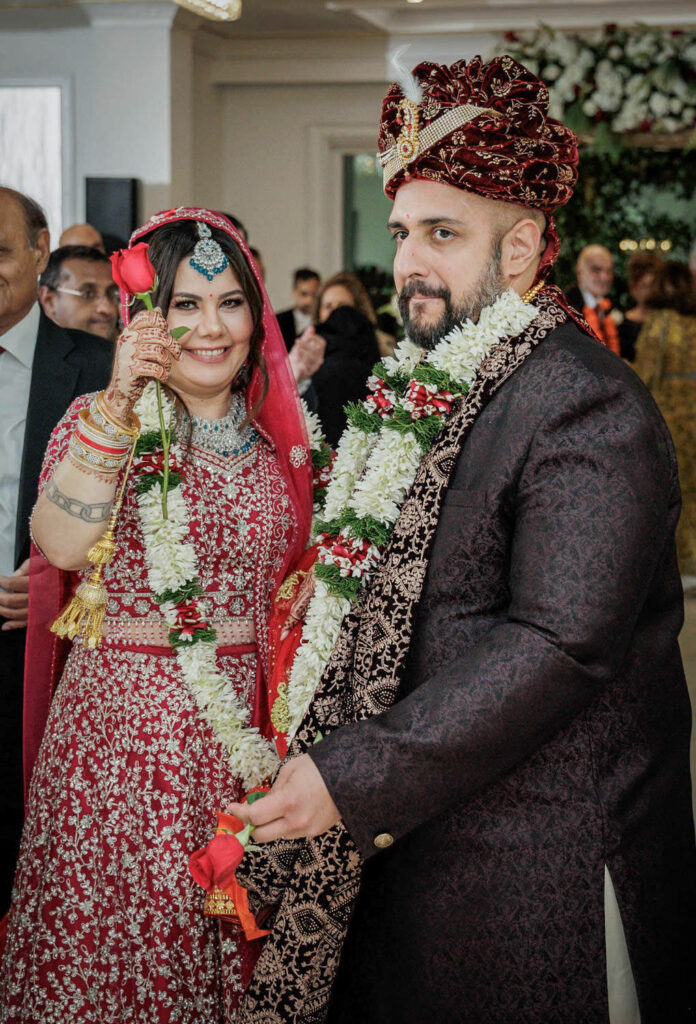 Joyful newlywed couple holding red roses after Hindu ceremony at Crystal Plaza New Jersey