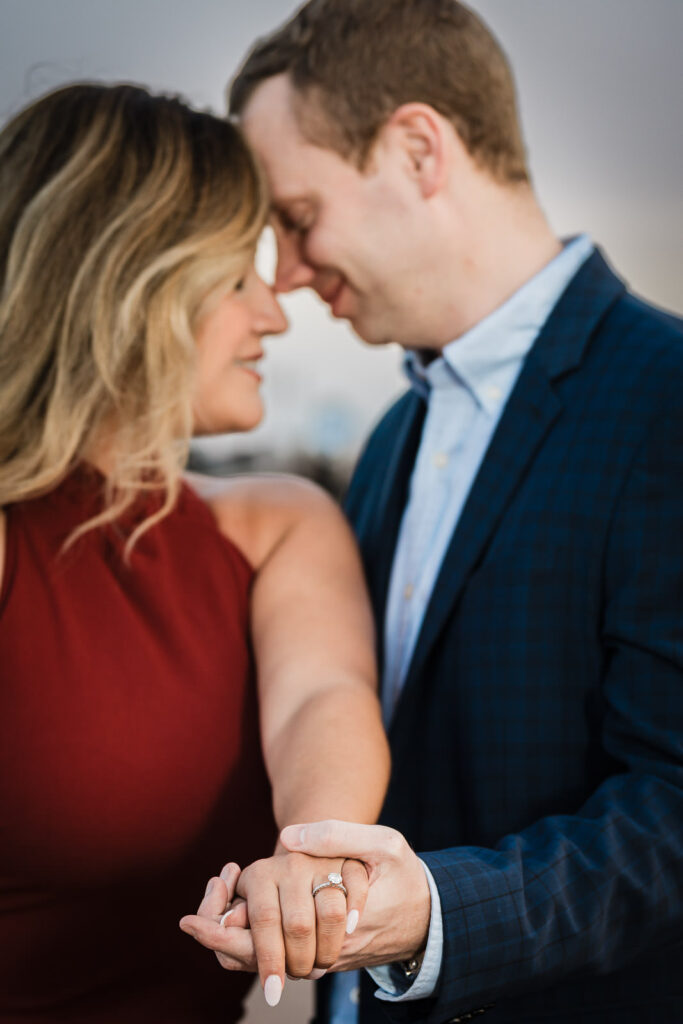 Close-up of engagement ring with couple nearly touching foreheads during Liberty State Park engagement session