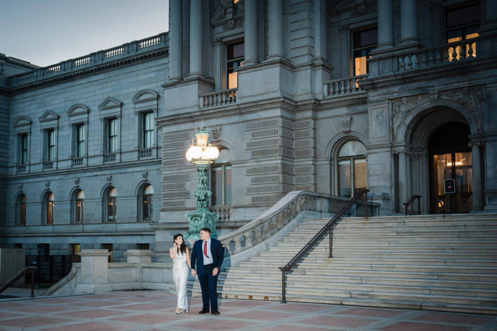 Couple walking hand in hand and laughing at the Library of Congress exterior at dusk Washington DC