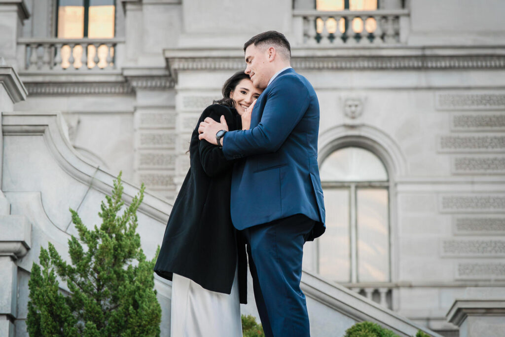 Woman smiling warmly while her partner holds her close on the Library of Congress steps