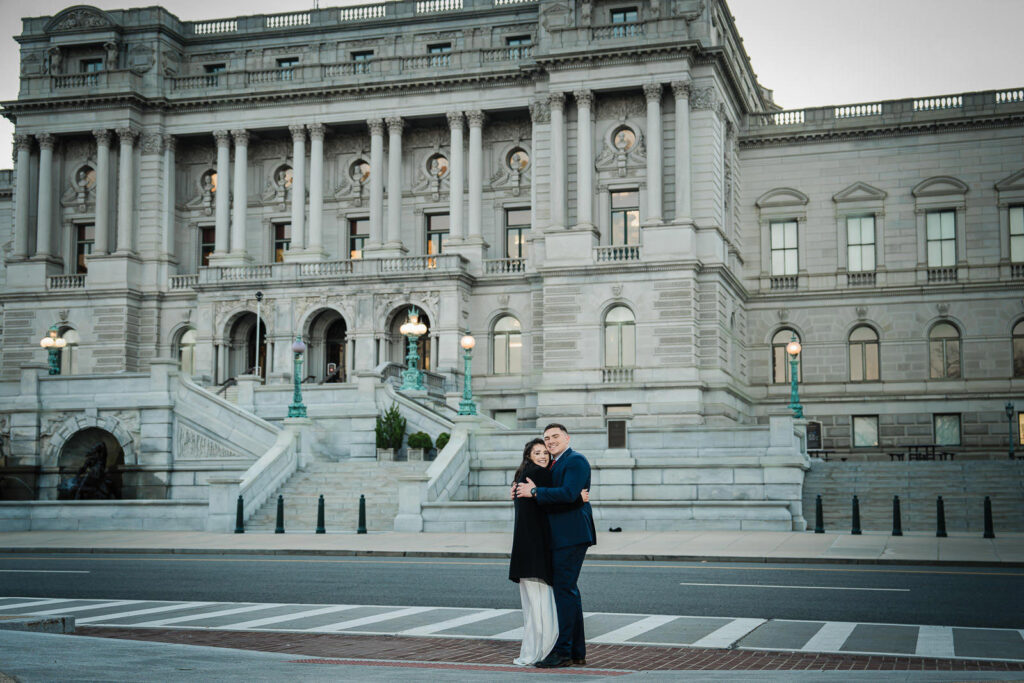 Couple embracing and smiling in front of the Library of Congress from across the street Washington DC