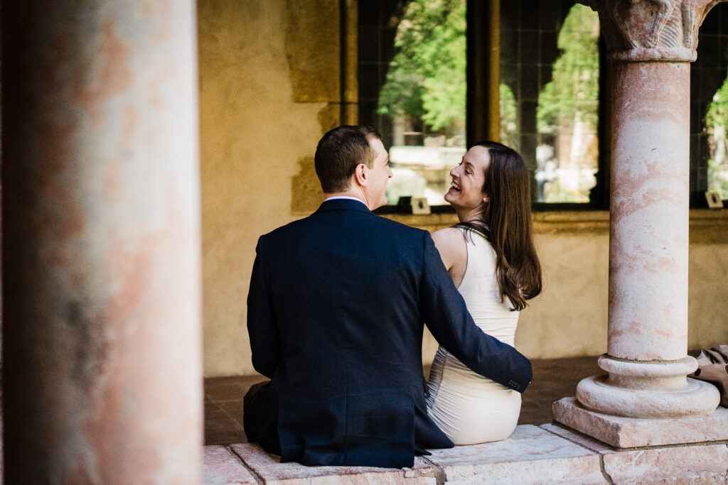 Newly engaged couple sitting and laughing together inside the stone arcade at The Met Cloisters