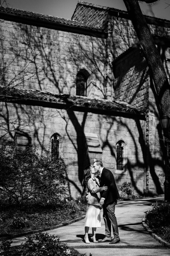 Black and white image of couple sharing a kiss outside the stone facade of The Met Cloisters