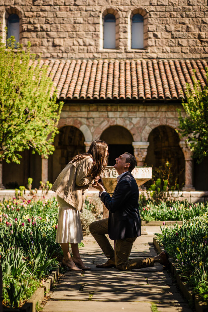 Couple sharing a joyful laugh immediately after a surprise proposal in the Cuxa Cloister garden