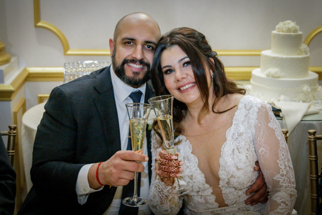 Newlywed couple toasting with champagne glasses at Crystal Plaza reception with wedding cake in background
